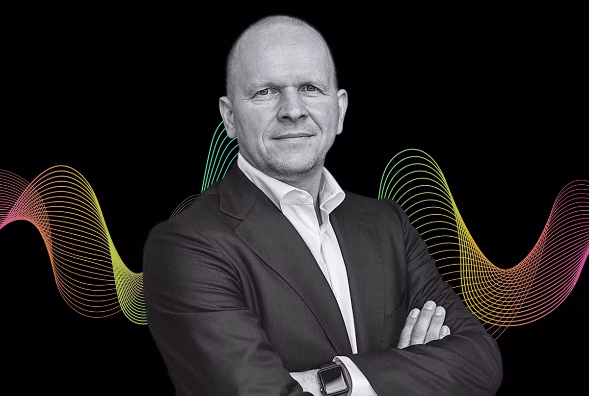 MasterCard CEO Michael Miebach in a suit with arms crossed, set against a black background with colorful wave patterns. Confident expression, wearing a smartwatch.