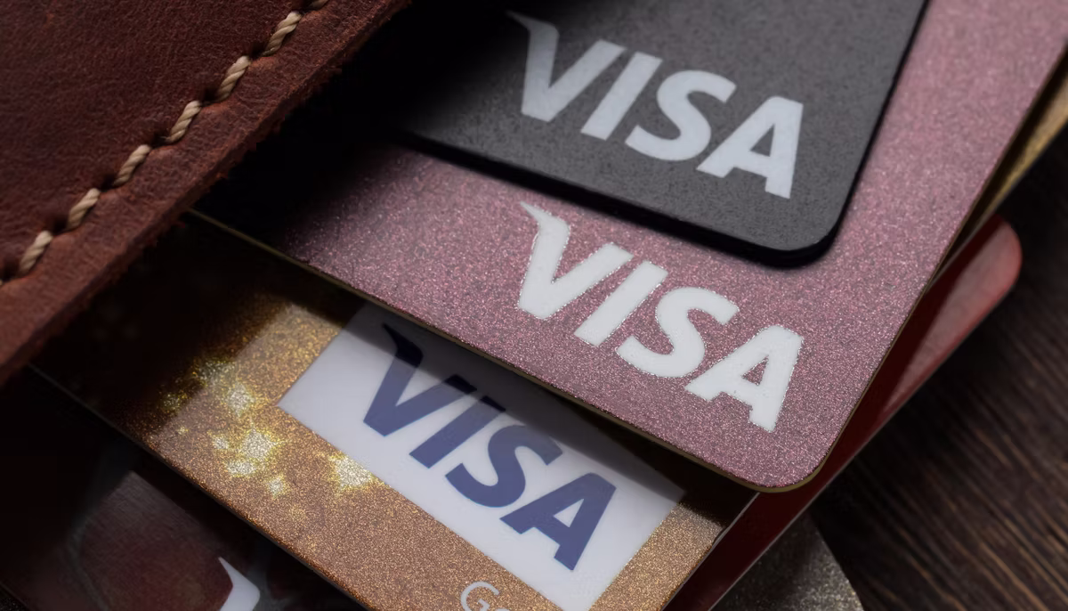 Close-up of several Visa cards in black, pink and gold fanned out of a brown leather wallet.
