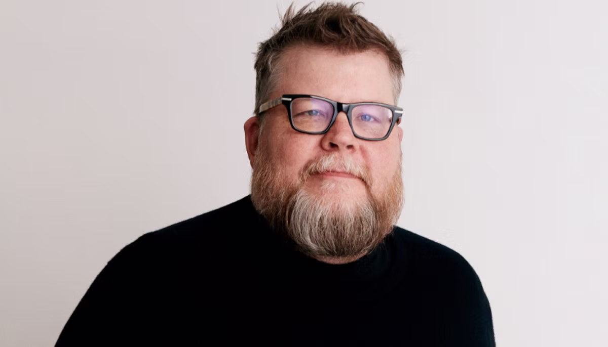 Etsy's Chief Product and Technology Officer Rafe Colburn a bearded man with glasses in a black shirt smiles slightly against a plain white background, exuding a calm and relaxed mood.